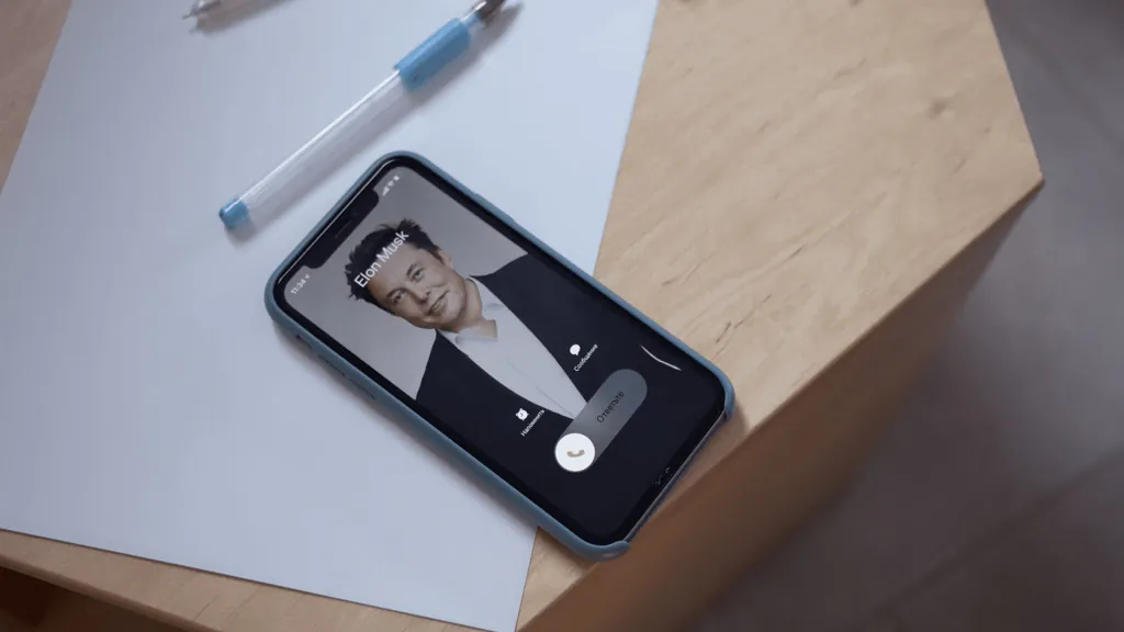 Iphone lying on hexagon wooden table with Elon Musk on screen
